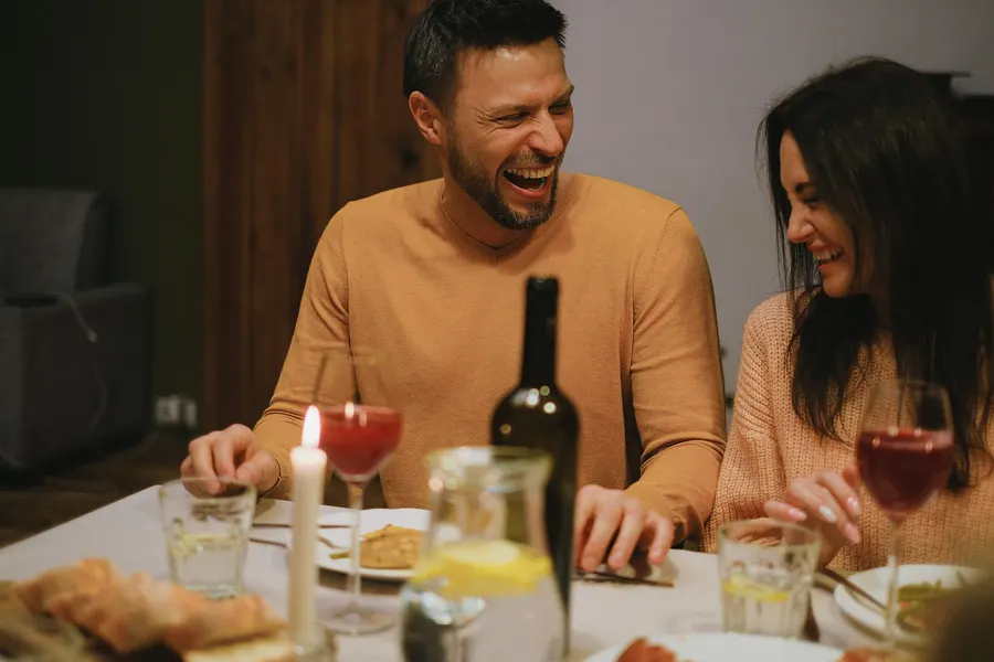 Two guests laughing over wine at a candlelit table