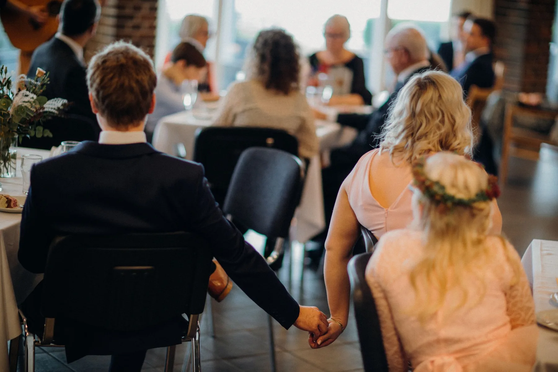 Two guests holding hands at a reception table while a speech goes on