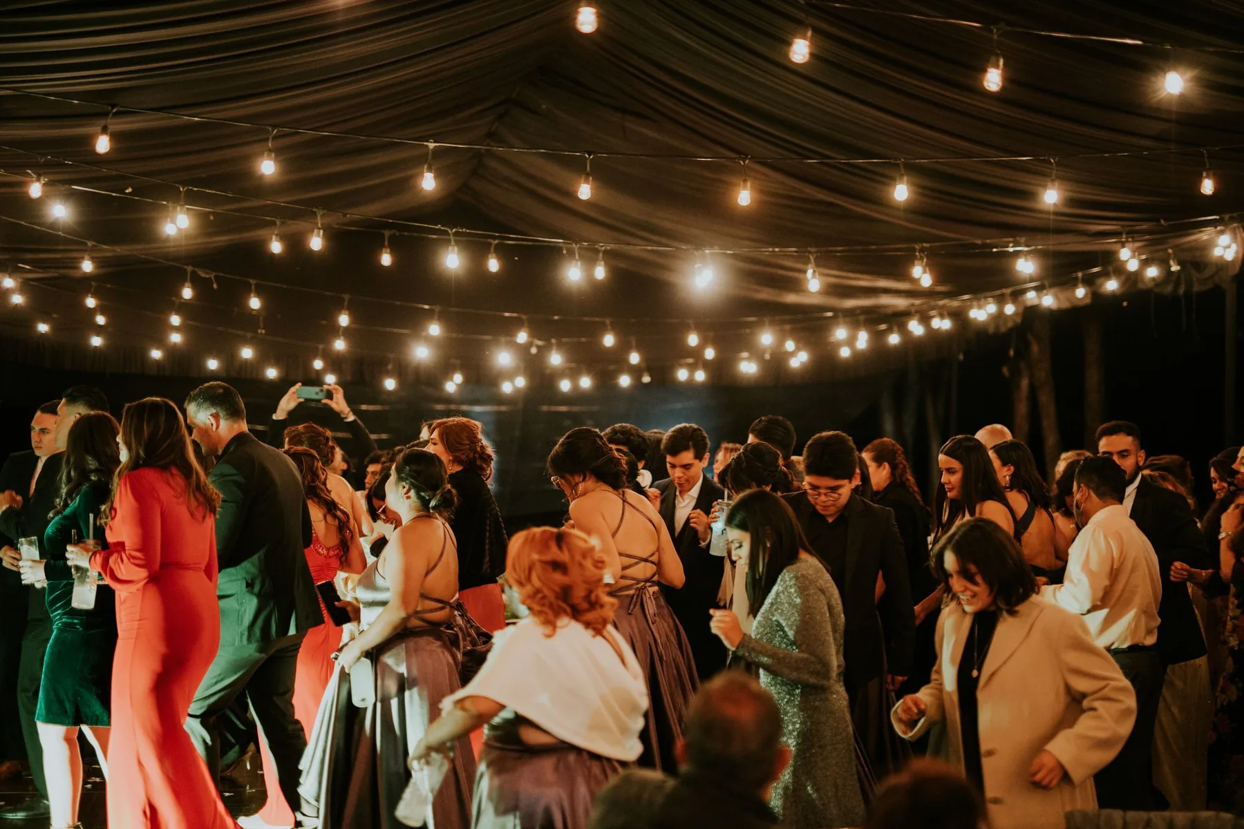 A marquee dance floor full of guests under strings of warm lights